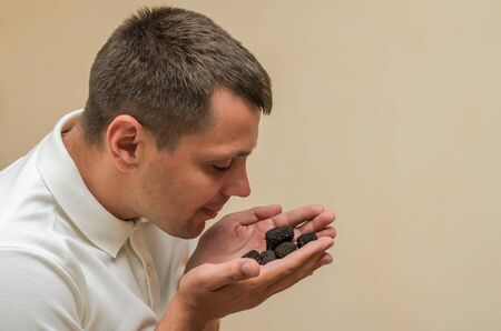 Young guy holding black truffle mushrooms in his hands on a light backgroundの写真素材