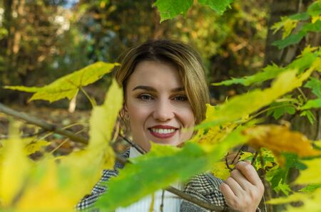 Young charming girl in autumn park among yellow maple leaves in autumn sunny day