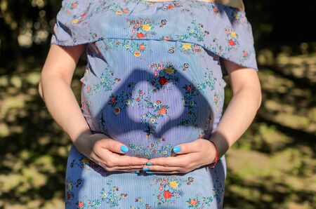 Heart-shaped shadow on the belly of a pregnant happy girl