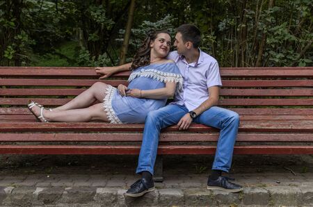 Young couple in love, husband and pregnant wife on a bench in the park, happy familyの写真素材