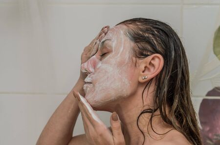 Young charming sexy girl makes a white scrub mask on her face in the bathroomの写真素材