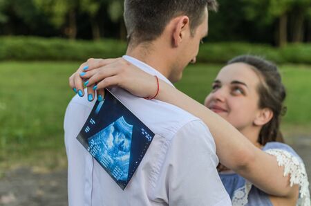 Young couple in love with a pregnant woman holds in their hands a picture of an ultrasound with an unborn babyの写真素材
