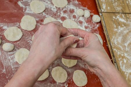 Woman cook sculpts dumplings from flour dough with potatoesの写真素材