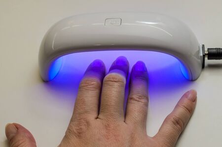 Woman dries gel nail polish under ultraviolet lampの写真素材
