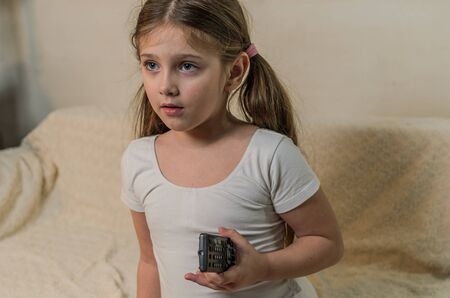 Little charming girl child sitting with TV channel remote controlの写真素材