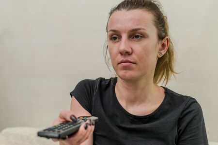 Young woman switches the television channels with the remote control
