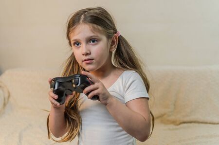 Little charming girl child plays a joystick in a video game on a game consoleの写真素材