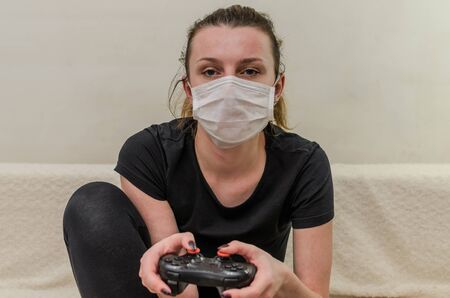 A young girl in a medical mask plays on a computer console using the joystick