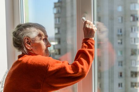 An elderly woman opens a window on a sunny dayの写真素材