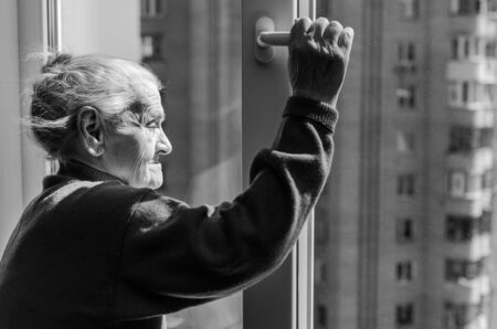 An elderly woman opens a window on a sunny dayの写真素材