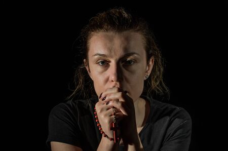 Young woman praying to god with prayer beads with a crucifix on the cross