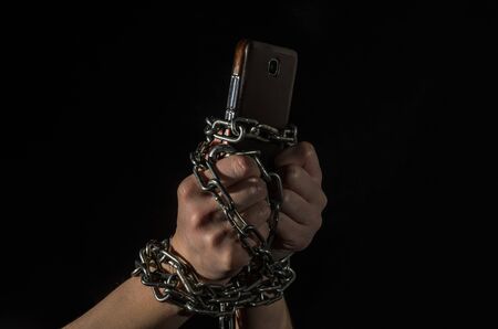 Human hands chained with a smartphone on a black backgroundの写真素材