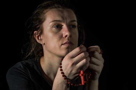 Young woman praying to god with prayer beads with a crucifix on the crossの写真素材