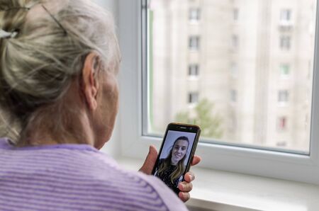 An elderly woman is talking via video calling on a smartphone with her young daughterの写真素材