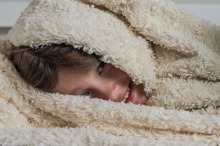 Little charming girl baby lying on the bed under the covers and smiling happyの写真素材