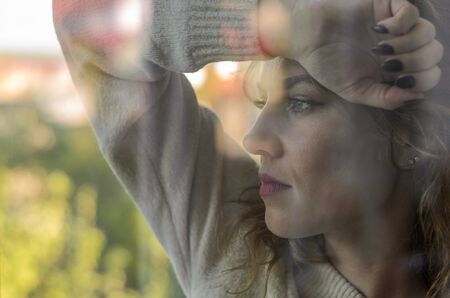 Young woman looking out of a window through a glass