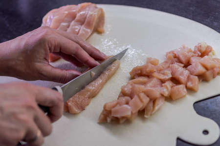 Chef cuts chicken breast with a knife on a cutting boardの写真素材