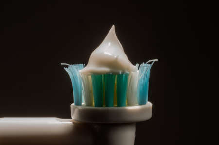 Macro shot of smearing toothpaste on electric toothbrush isolated on black background