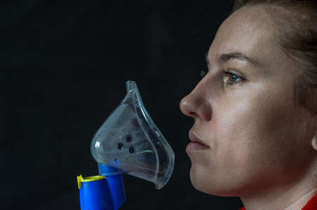Woman breathing into mask while making inhalation on black backgroundの写真素材