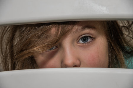 Little adorable girl child looks through a crack in a hole in a wooden fenceの写真素材