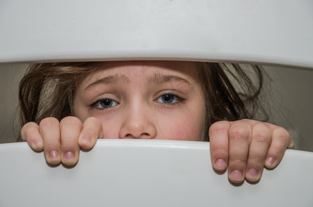 Little adorable girl child looks through a crack in a hole in a wooden fenceの写真素材