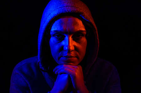 Portrait of a young woman in a hood, in red and blue light, isolated on a black backgroundの写真素材