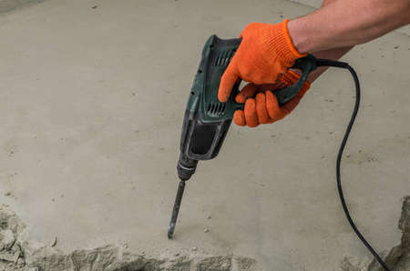 A builder dismantles a perforator drill breaks the concrete floor at a construction site