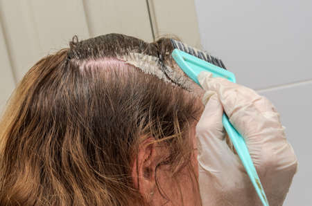 Young beautiful woman herself dyes her hair with paint and a brushの写真素材