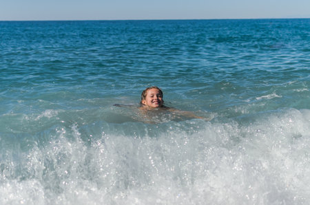 Little happy adorable girl child swims in the sea and plays on the waves during the holidays on the sea coastの写真素材