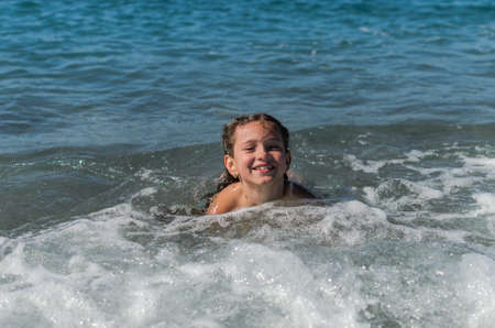 Little happy adorable girl child swims in the sea and plays on the waves during the holidays on the sea coastの写真素材