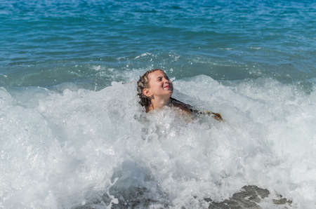 Little happy adorable girl child swims in the sea and plays on the waves during the holidays on the sea coastの写真素材