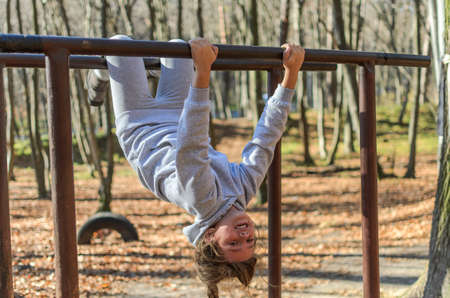 Little adorable girl child in a tracksuit trains on horizontal bars on the street in the autumn forestの写真素材