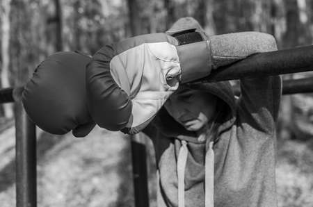 Young charming woman, in a tracksuit with a hood on her head, in red boxing gloves, is resting after training in women's boxing in the autumn forest in natureの写真素材