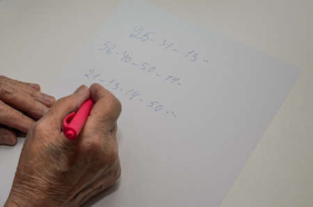 The hand of an elderly woman writes numbers with a pen on a piece of paper