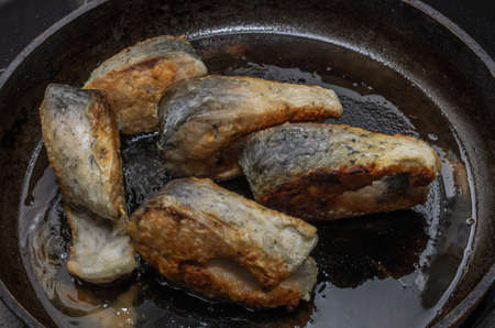 The cook fries carp fish in a frying pan on an induction stove