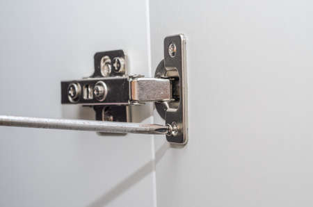 The furniture maker installs furniture hinges in the closet, tightening the screw with a screwdriverの写真素材