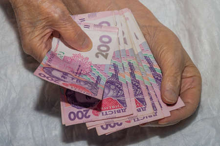 The hands of an elderly woman hold Ukrainian hryvnia money in bills of 200 hryvnia