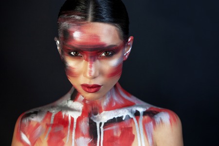 close-up Eurasian girls with dark hair and clear skin, and brown eyes, on a black background, in makeup red ottenkami on the face in the form of strokes, and delicate red lipsの写真素材