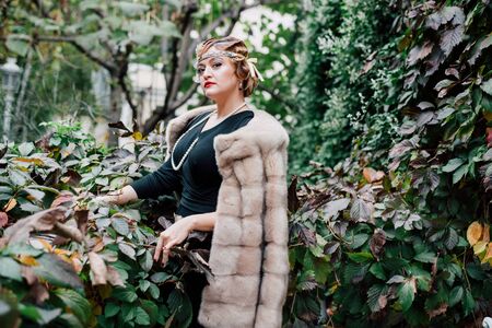 a gorgeous woman in a fur cape is surrounded by green ivy on her head a tiara, a bead hairstyle hangs on her neckの写真素材