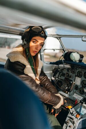 close-up of a pilot s girl in the cockpit of an airplane with a dashboard, a helmet and goggles on her head, and a beam of light falling on her face artificially, striking her emotions of confidenceの写真素材