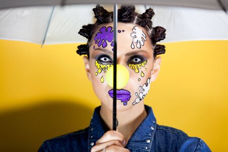 girl on a yellow background with makeup in the form of colored spots, pleasantly looking at the...