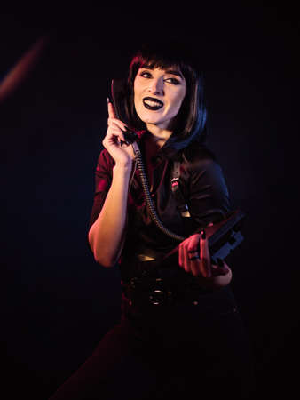 The girl on a black background smiles and looks to the side. In her hands she holds a telephone set,...
