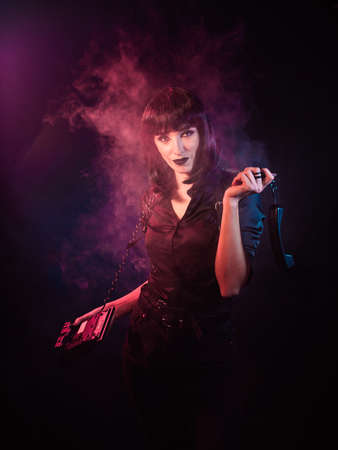 girl on a black background with pink-blue light and a slight haze. She is holding a telephone in her...