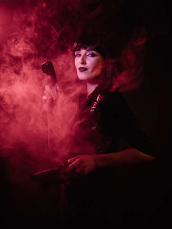 a girl in a harness in red light and smoke looks at the camera and holds a phone receiver in her handsの写真素材