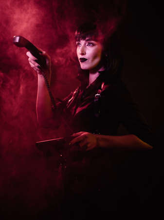 girl in a harness with black hair and a shirt in red light and smoke, points and looks to the sideの写真素材