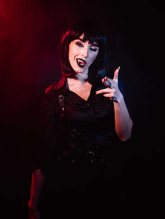 Girl on a black background with red-blue light in the form of a vampire. She winks and gestures with her hands to the camera while showing her fangs.の写真素材