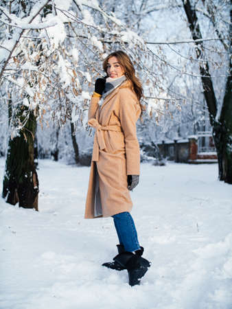 girl against the background of the bright sun and frozen tree branches in a beige coat in the parkの写真素材