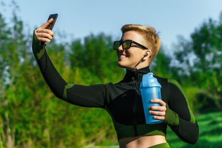 Nice sports woman makes selfie while joggingの写真素材
