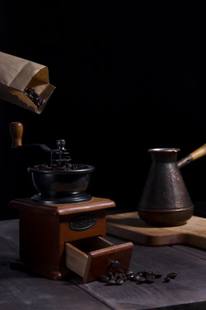 Pouring coffee grains from paper package into coffee grinder with Cezve on the black backgroundの写真素材