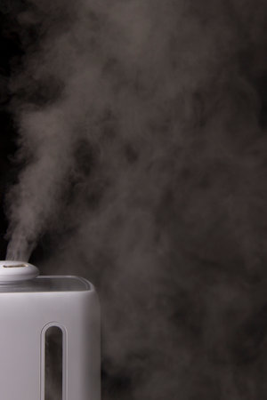 White modern humidifier with seen rest of water creates white steam on black backgroundの写真素材